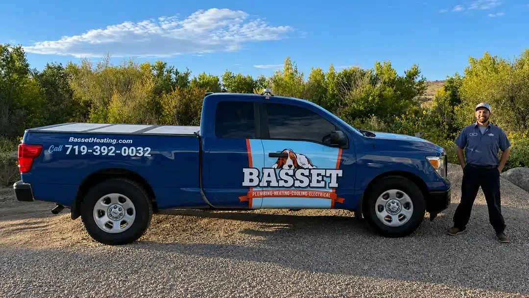 Professional BASSETT technician standing beside electrical and heating service truck in Colorado Springs landscape